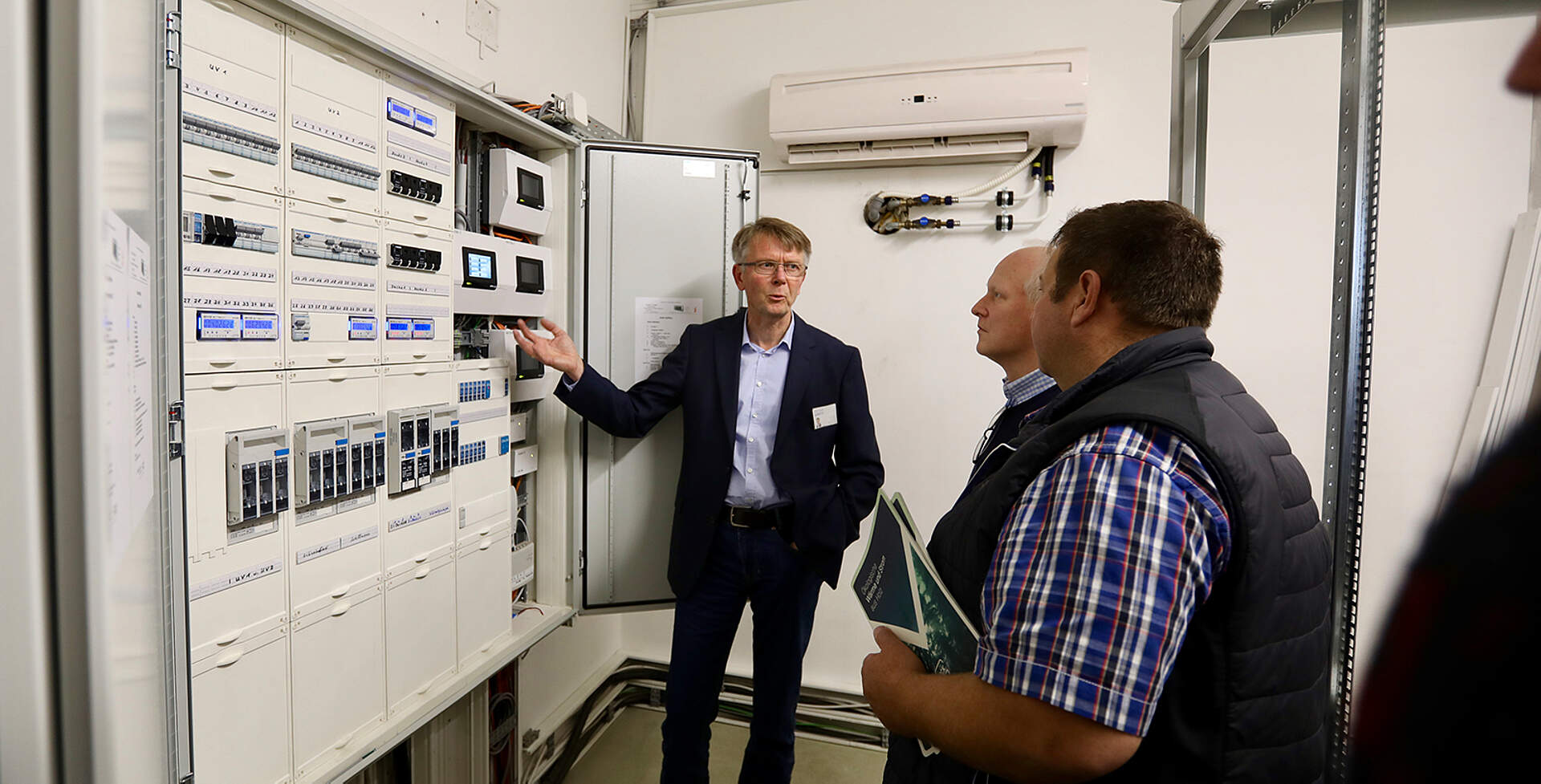 Stephan Janbeck erklärt die Regeltechnik zwei Besuchern beim Energie-Workshop