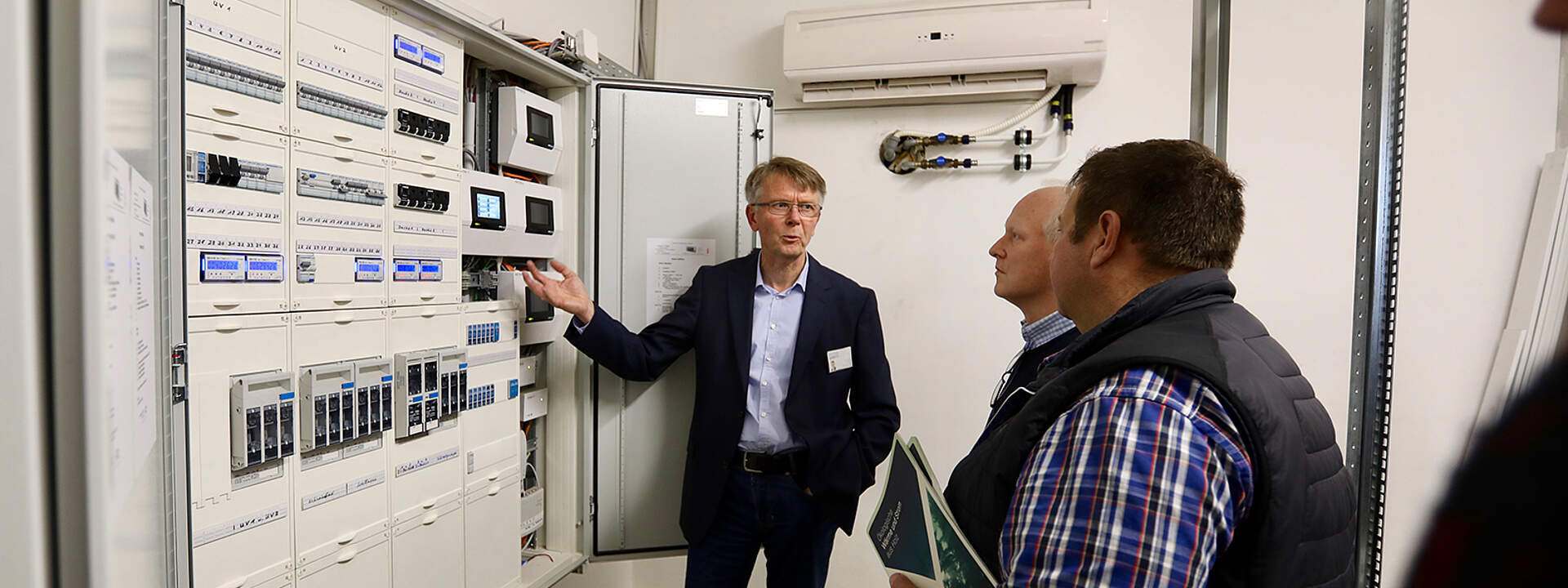 Stephan Janbeck erklärt die Regeltechnik zwei Besuchern beim Energie-Workshop